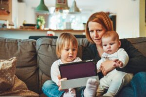 mother watching tablet with toddler and infant