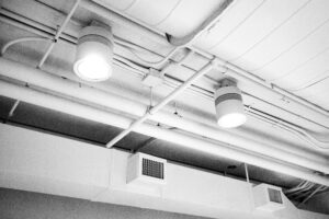 white ceiling with exposed air ducts and florescent lighting