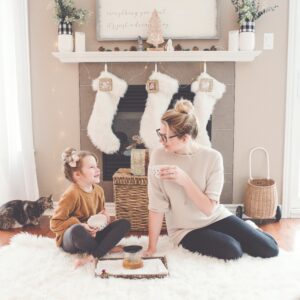 Mom and daughter drinking coffee on a carpet in front of the fireplace with white stockings hung